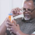 A senior African-American couple in their 60s sitting at a table at home looking at the label of a bottle of prescription medicine, trying to figure out what dose to take.