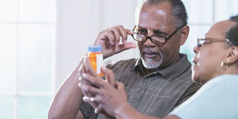 A senior African-American couple in their 60s sitting at a table at home looking at the label of a bottle of prescription medicine, trying to figure out what dose to take.