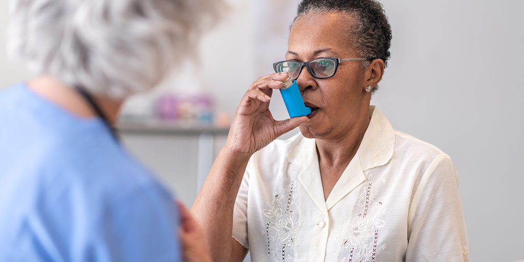 A senior black women with asthma is learning how to use an inhaler. The female doctor is showing her how to use the asthma inhaler.